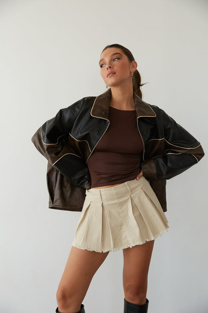 A lady in a leather jacket, brown top, and pleated skirt from American Threads, showing a cute fall outfit.